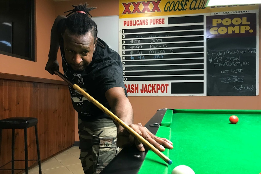 A man with dreadlocks plays pool in a pub.