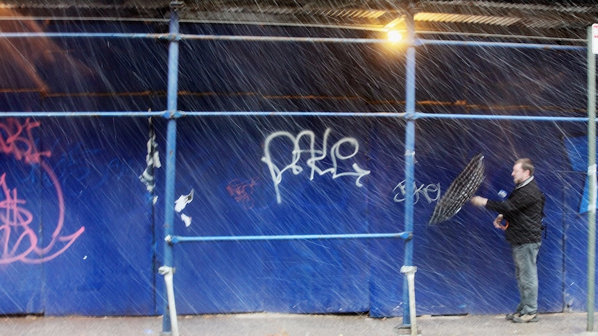 A man attempts to fix his umbrella while walking through snow in Manhattan