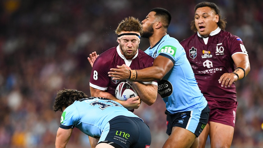 Christian Welch has his eyes closed as he is tackled by two New South Wales players