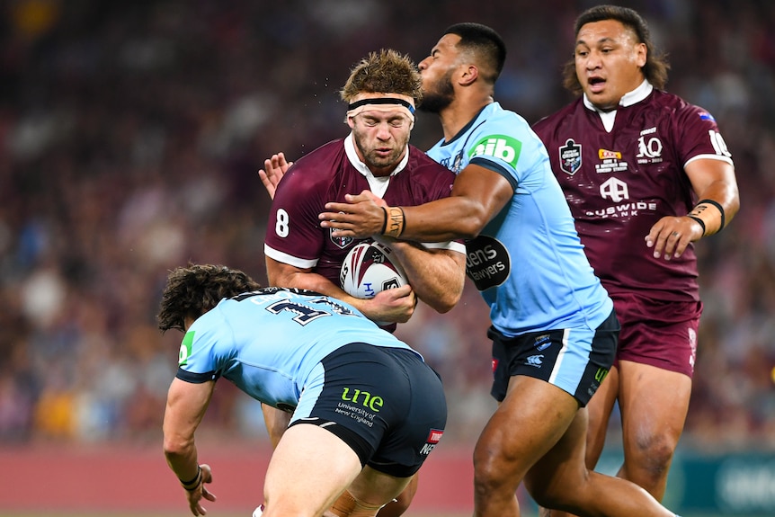 Christian Welch has his eyes closed as he is tackled by two New South Wales players