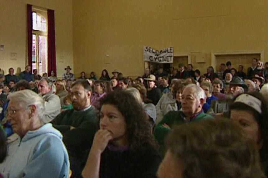 A grainy image taken from a 1995 TV story showing a crowd at the Cygnet Town Hall and a sign reading 'self rule for Cygnet'