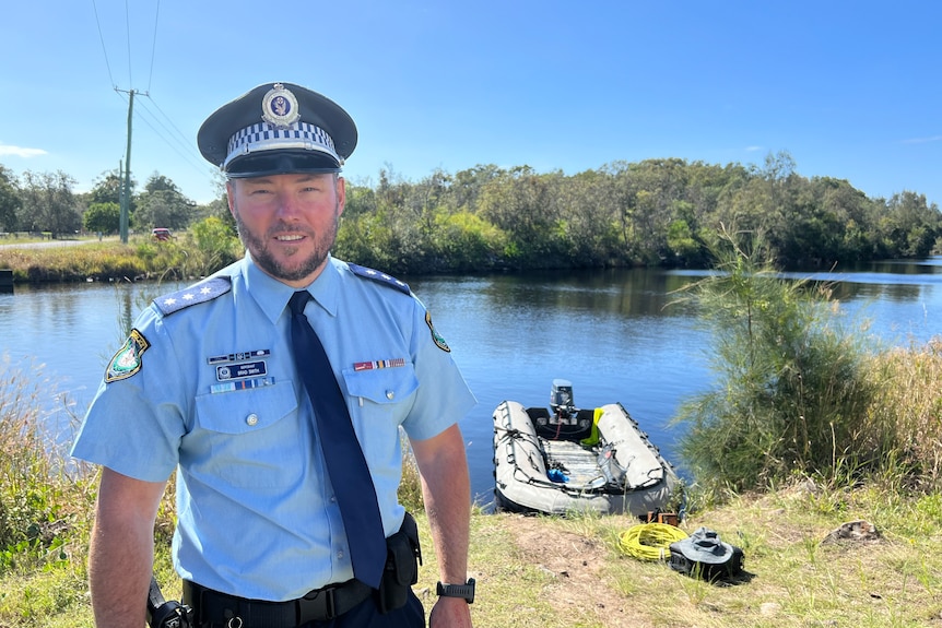 Police officer standing on banks of waterway with small police boat in background