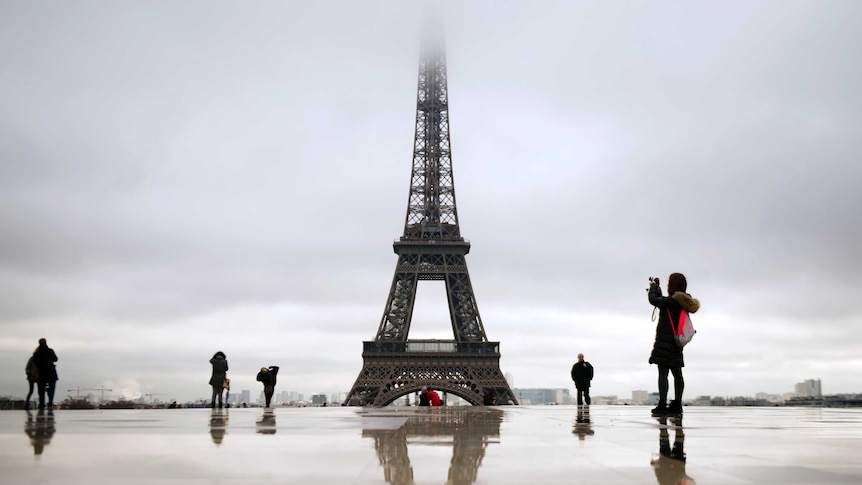 People walk on the Trocadero square as the top of the Eiffel tower is taken in the mist on December 7, 2012 in Paris.