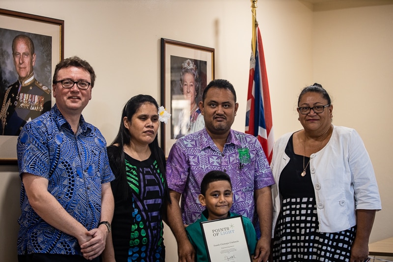 A woman standing with two men, a women and a child receiving an award. 