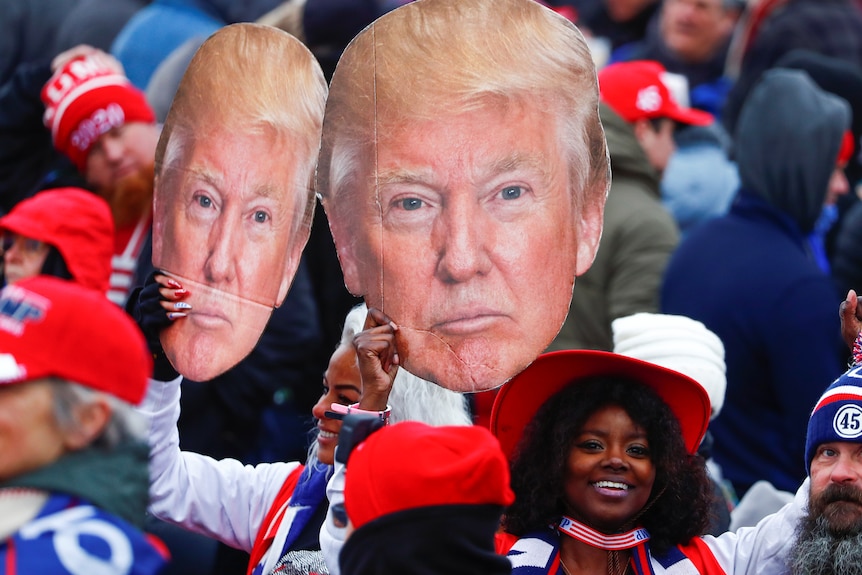 Two women dressed in Trump merchandise hold up signs of the former president's face while at a rally on January 6