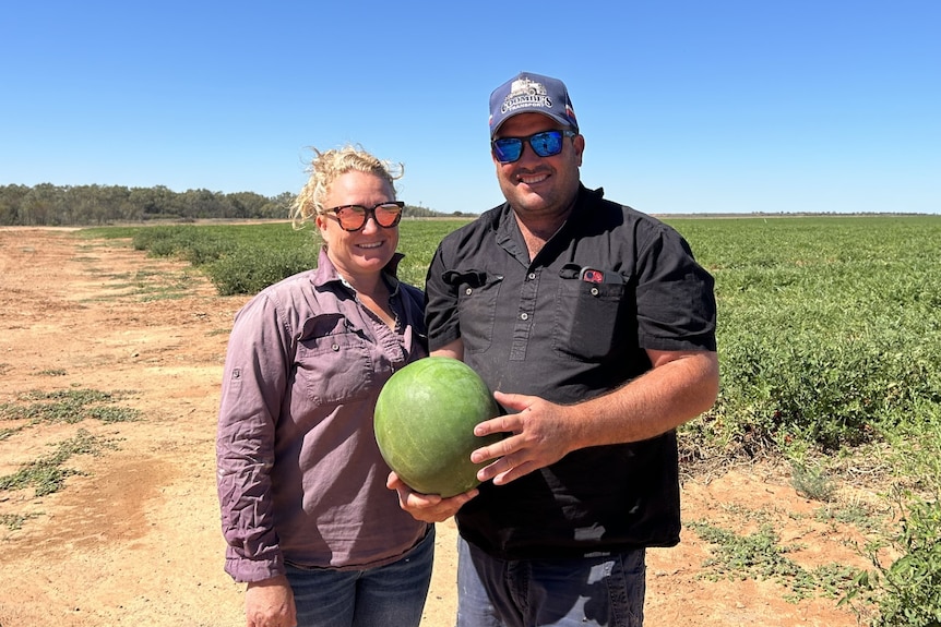 A couple stand on a paddock holding a watermelon