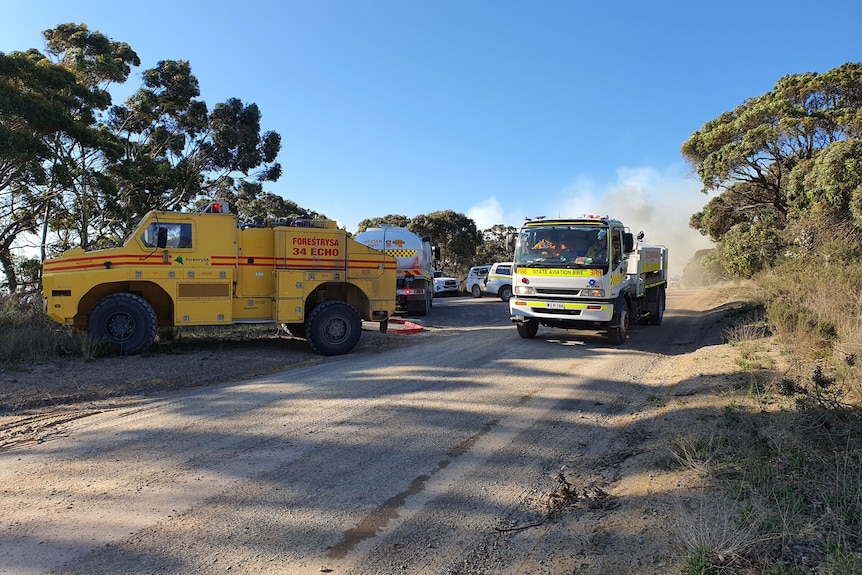 Firefighting vehicles parked on a road with smoke behind