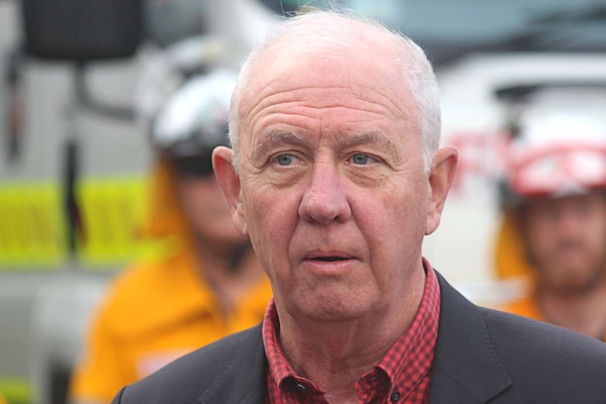 A man in a suit stands behind emergency service workers