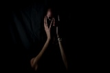 Generic, anonymous photo of woman in darkness holding hands over her face