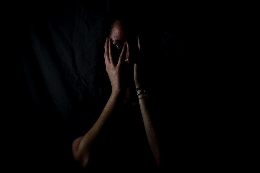 Generic, anonymous photo of woman in darkness holding hands over her face