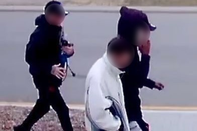 Three young men walk on the street. One appears to carry a power tool.