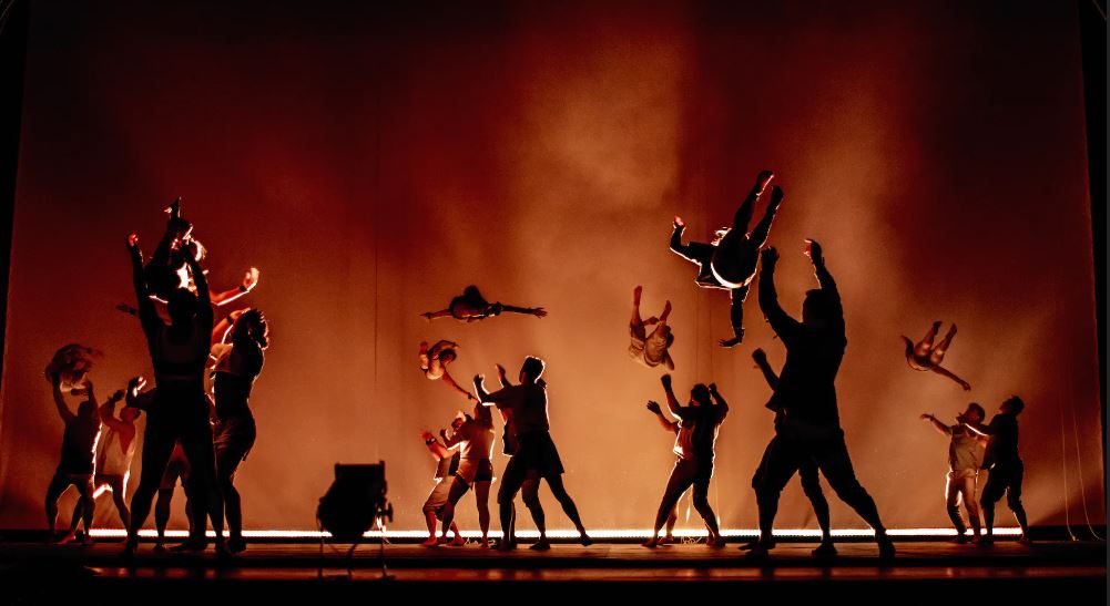 acrobats in silhouette with some performers in the air with orange background
