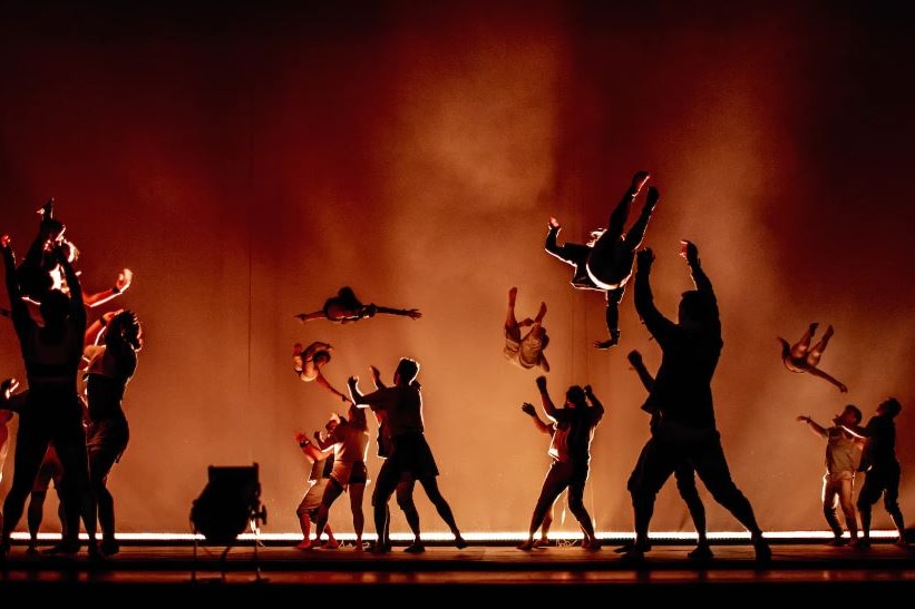 acrobats in silhouette with some performers in the air with orange background