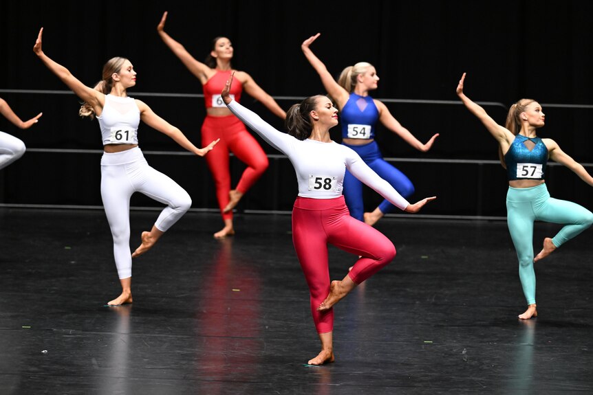 Young women dancers perform on a stage, in bright coloured tights and crop tops.