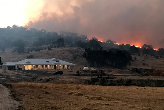 A bushfire burning on a hill behind a house.