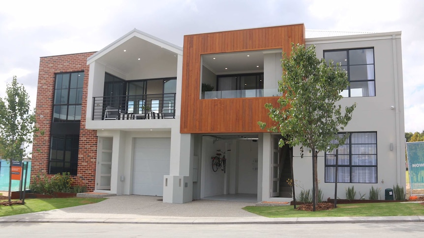 A small, new two-storey display home in a housing estate with landscaping viewed from across the road.