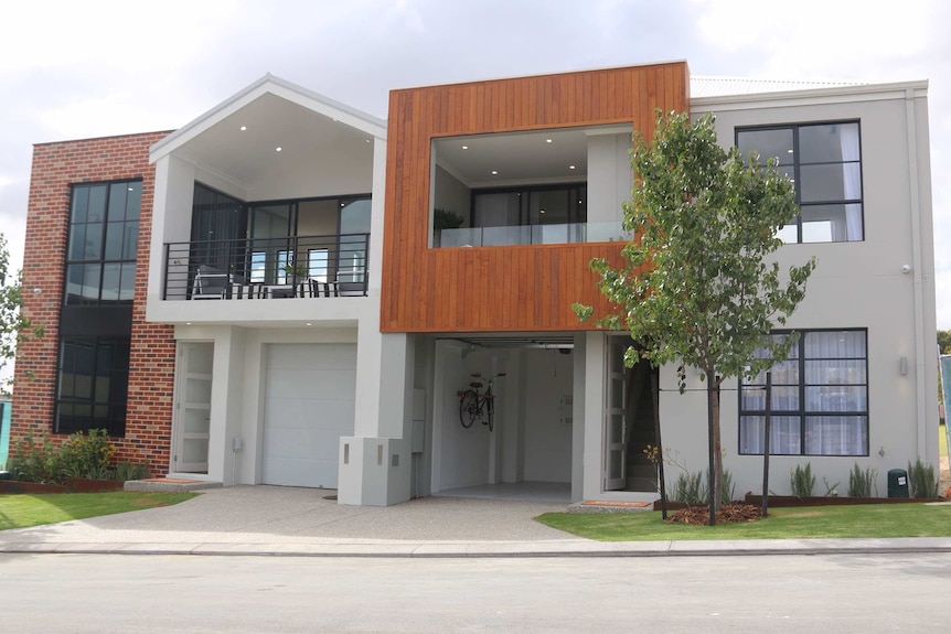 A small, new two-storey display home in a housing estate with landscaping viewed from across the road.