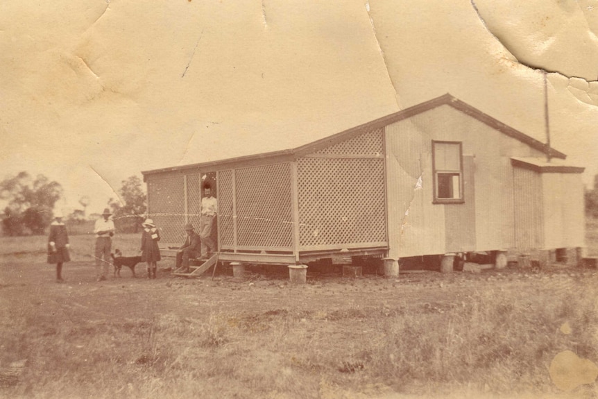 A sepia photograph of the original Mentone homestead around 1914. Five people standing at the front of the tin structure.