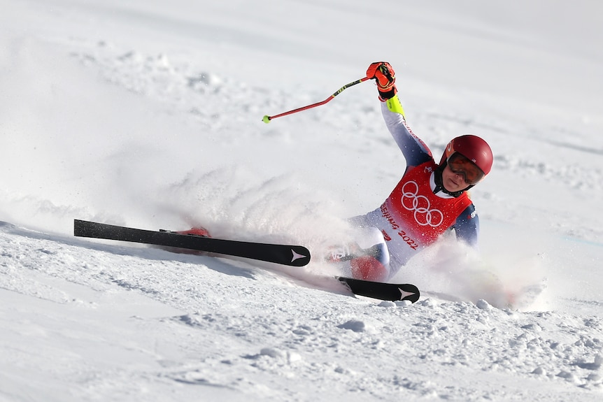 A skiier slides in the snow with her pole in the air after missing a turn on a hill