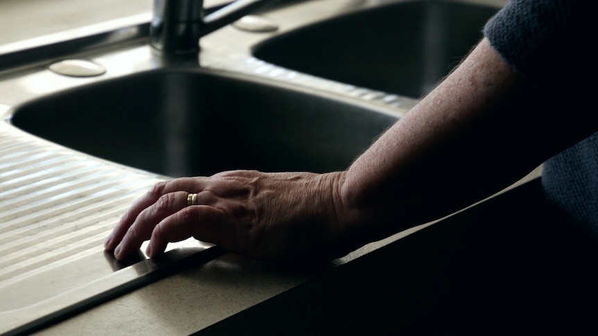 A woman's hand rests on a stainless steel kitchen sink.