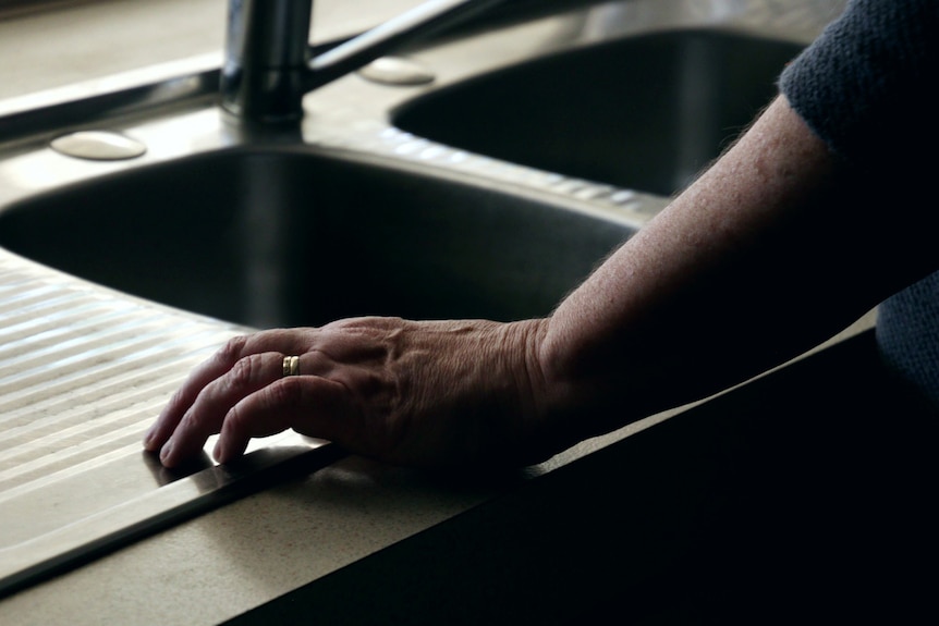 A woman's hand rests on a stainless steel kitchen sink.