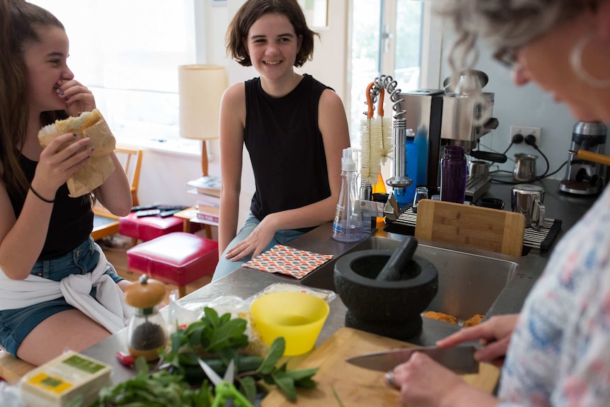 Xenia's daughters sit at the kitchen bench chatting to their mother as Xenia prepares dinner.