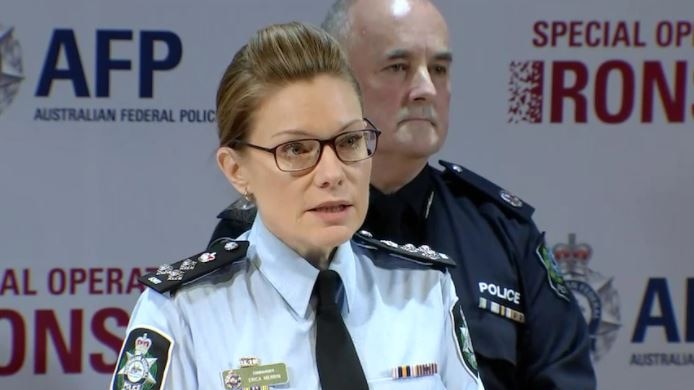 A woman in a police uniform, standing in front of a man in a police uniform.