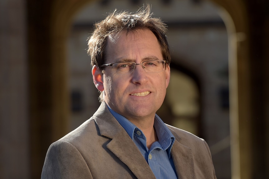 Roger Wilkins, a man with brown hair and glasses, smiles for a photo.