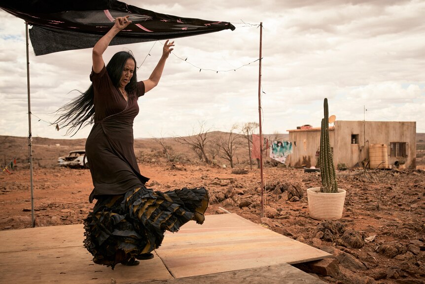 A woman in a flamenco dress dances with a desert behind her. 