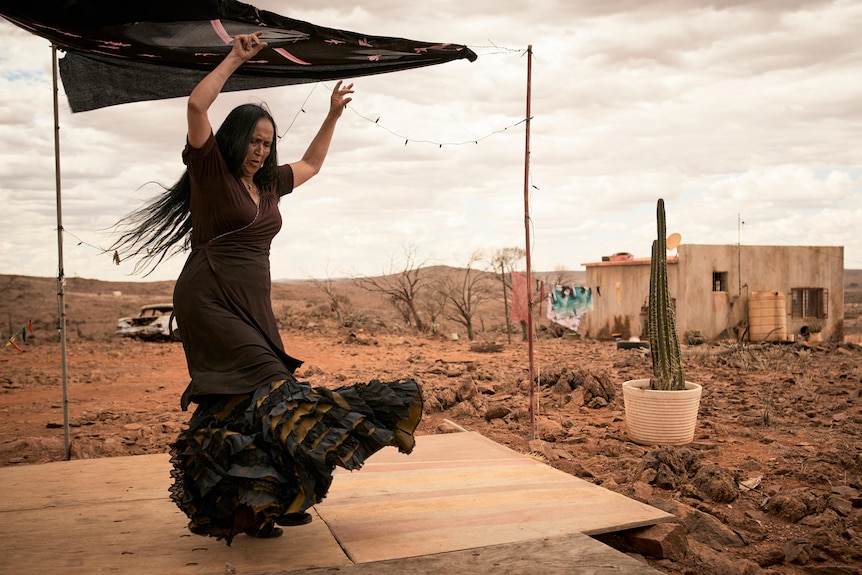 A woman in a flamenco dress dances with a desert behind her. 