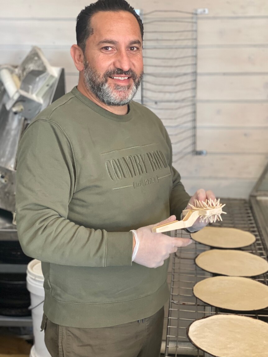 A man stands in front of a tray where he's making flatbread.