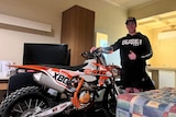 boy standing next to orange and white dirt bike, giving thumbs up