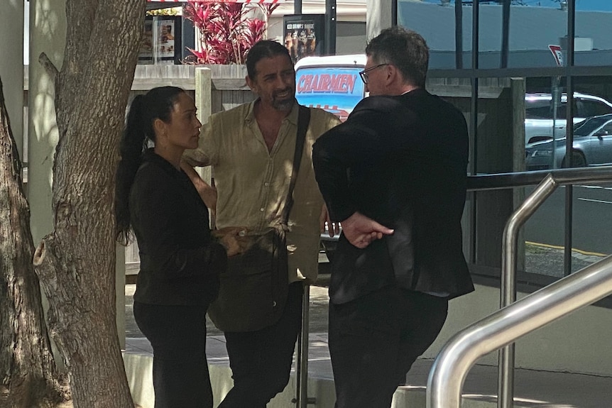 A woman stands with two men in front of building.