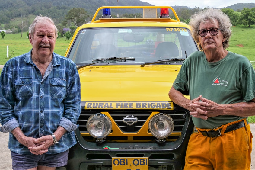 two elderly men leaning up against yellow rural fire service truck 