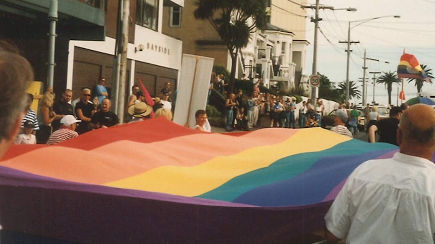 A rainbow flag being carried down a street.