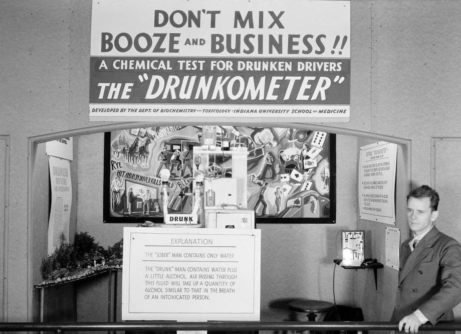 A man stands in front of a sign that says 'Drunkometer'.