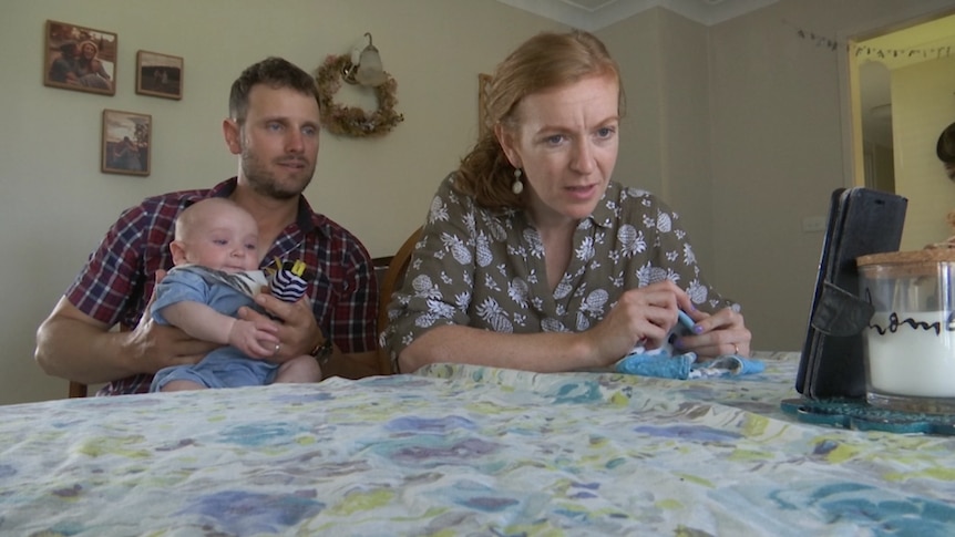 A man, woman and baby sitting at a table looking at a phone.
