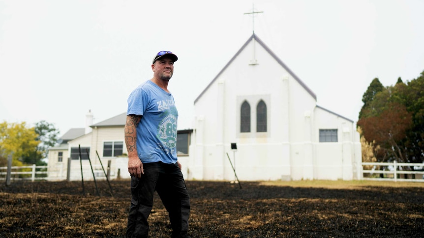 A man stands on burnt grass in front of an old church