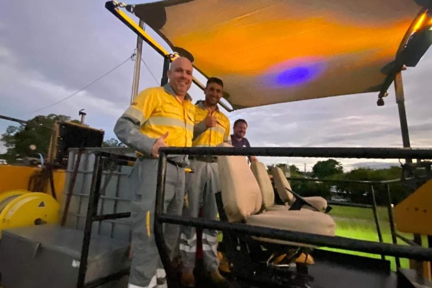 men in high vis uniforms stand on a small train smiling 