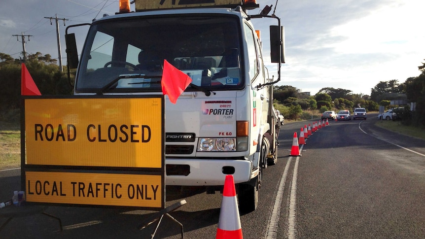 Road closed sign in front of a truck on a road near bushfires, not visible, at Skenes Creek.