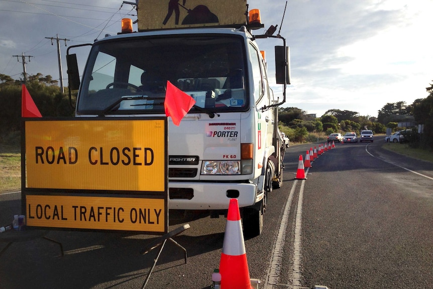 Road closed sign in front of a truck on a road near bushfires, not visible, at Skenes Creek.