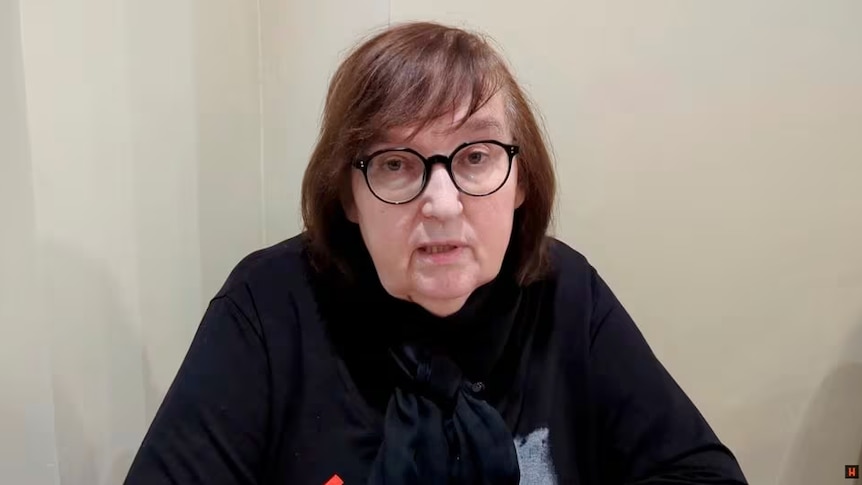 A woman wearing black and wearing glasses talking to the camera