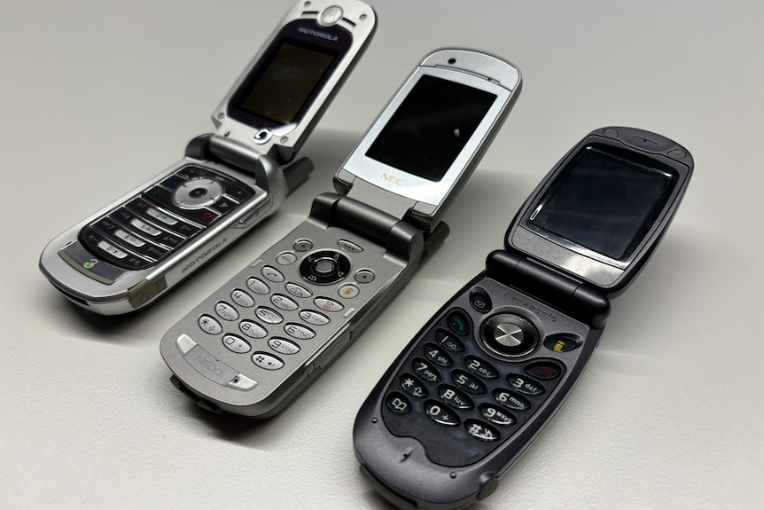 A close up of three flip phones open and sitting on a table.