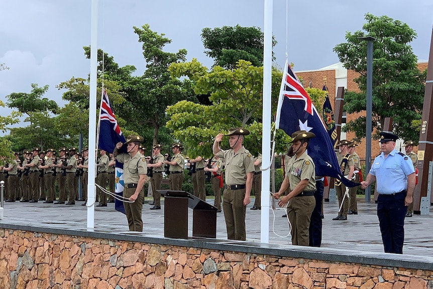 Soldiers salute as flags are raised at military barracks.