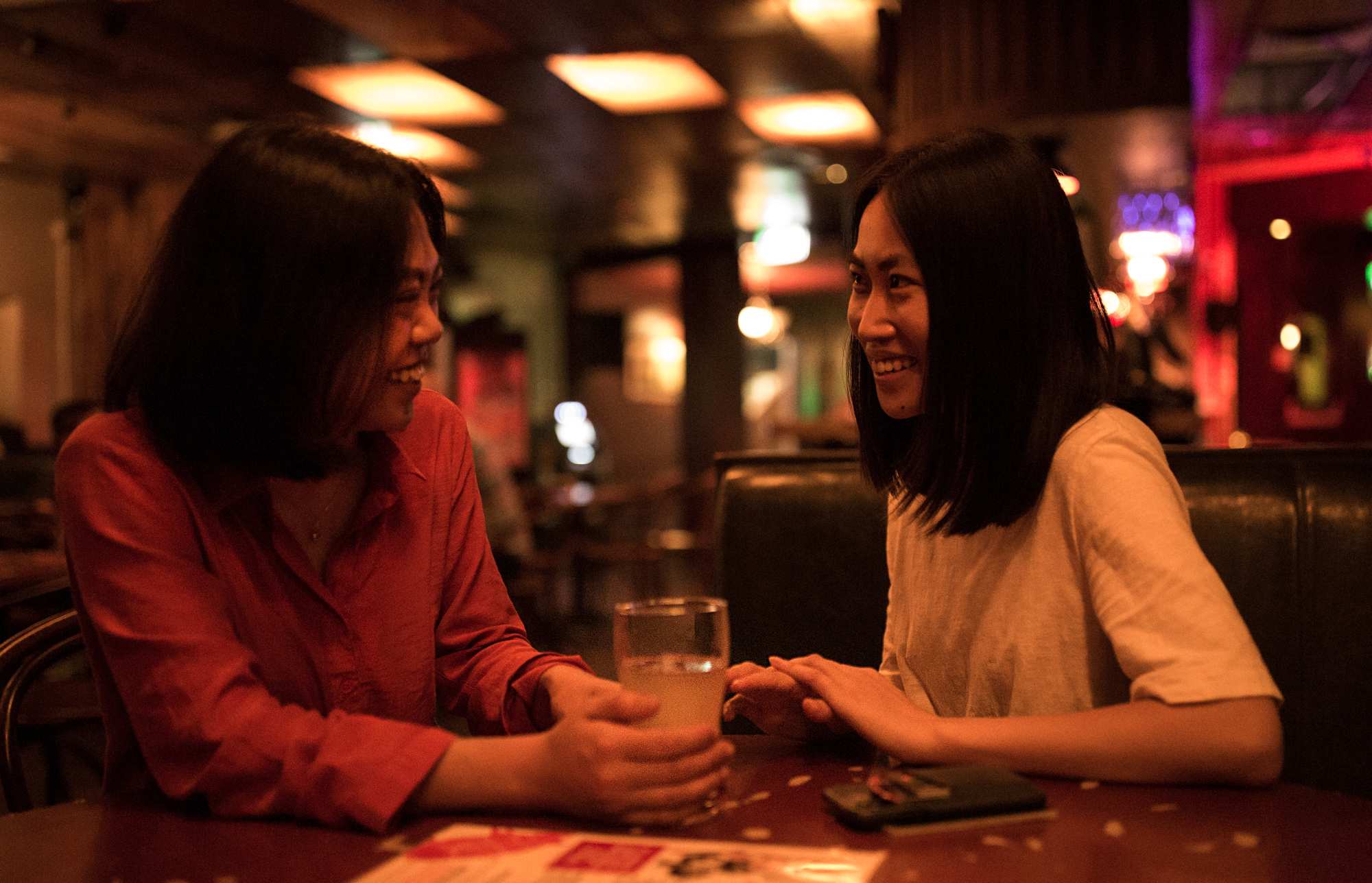 two women sitting down and smiling at each other in a bar