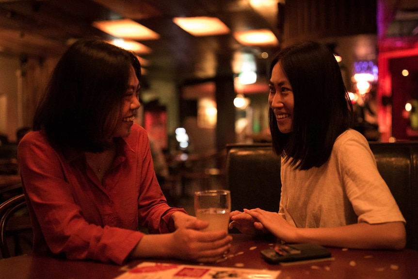 two women sitting down and smiling at each other in a bar