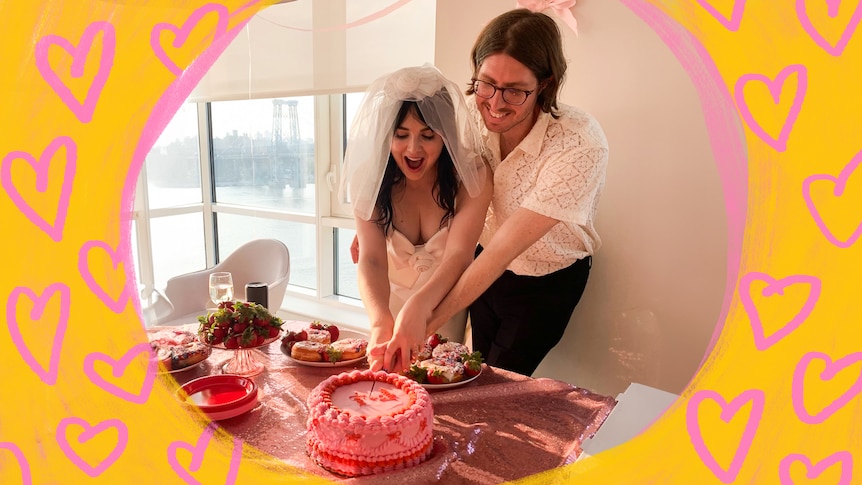 Emily, left, wears a white wedding dress and veil as she cuts a pink and red cake with Tom, right, both smiling.