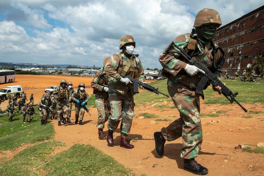 South African National Defence Forces soldiers run towards a neighbourhood with surgical masks on.