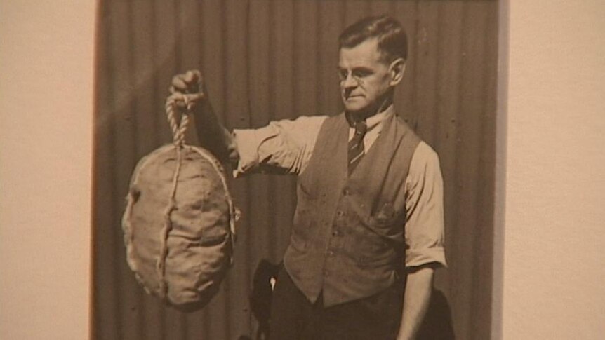 Man holding up unidentified object tied with rope. 1925. Unknown photographer.