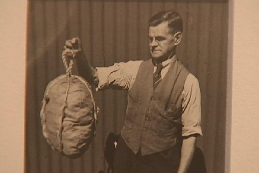 Man holding up unidentified object tied with rope. 1925. Unknown photographer.